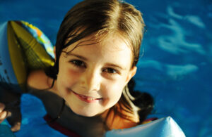 Little cute girl in blue water of the swimming pool, summer time for fun