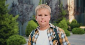 close up of pensive caucasian schoolboy with backpack posing and looking at camera in SBI 351232009